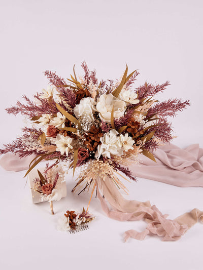 hair comb is lying on white background near boutonniere and standing wedding bouquet with dusty ribbon near dusty pink fabric