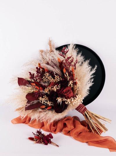 boutonniere is lying on white background near wedding bouquet on terracota organza