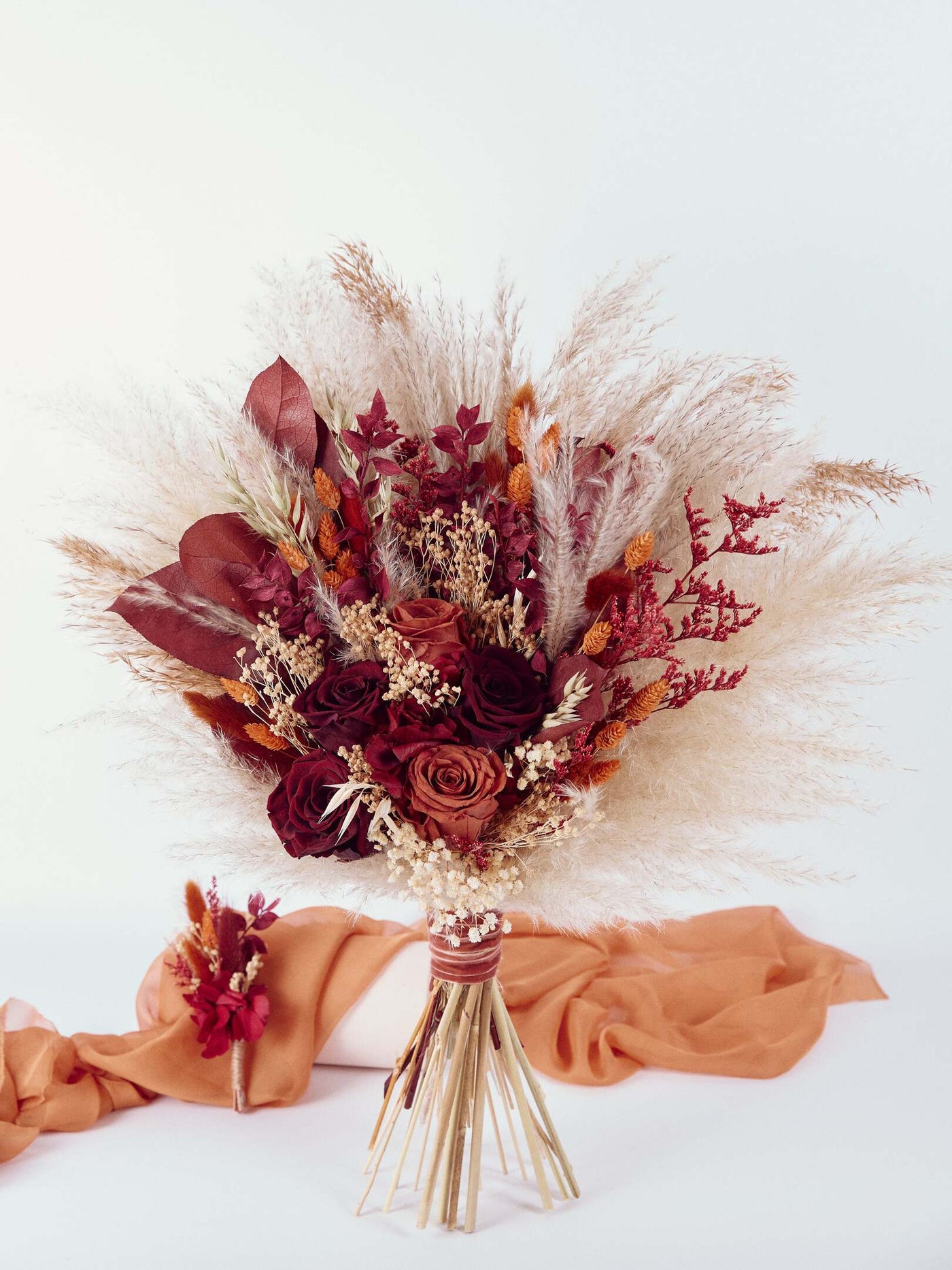 boutonniere is supported on a terracotta organza near a wedding bouquet on white background