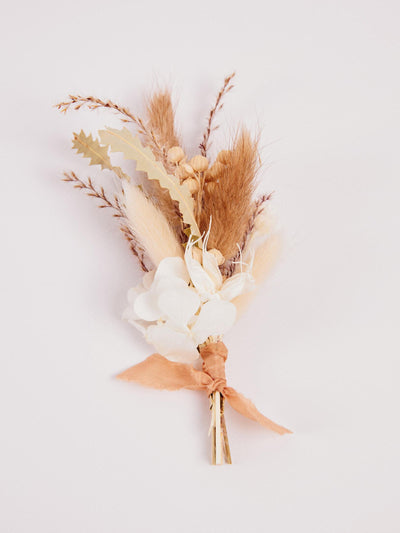 boutonniere with pampas grass, branches and cream ribbon on white background