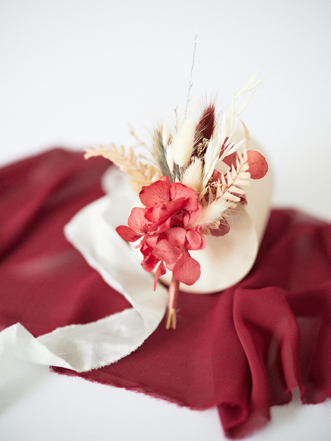 the boutonniere is propped up on a white stand on a burgundy fabric