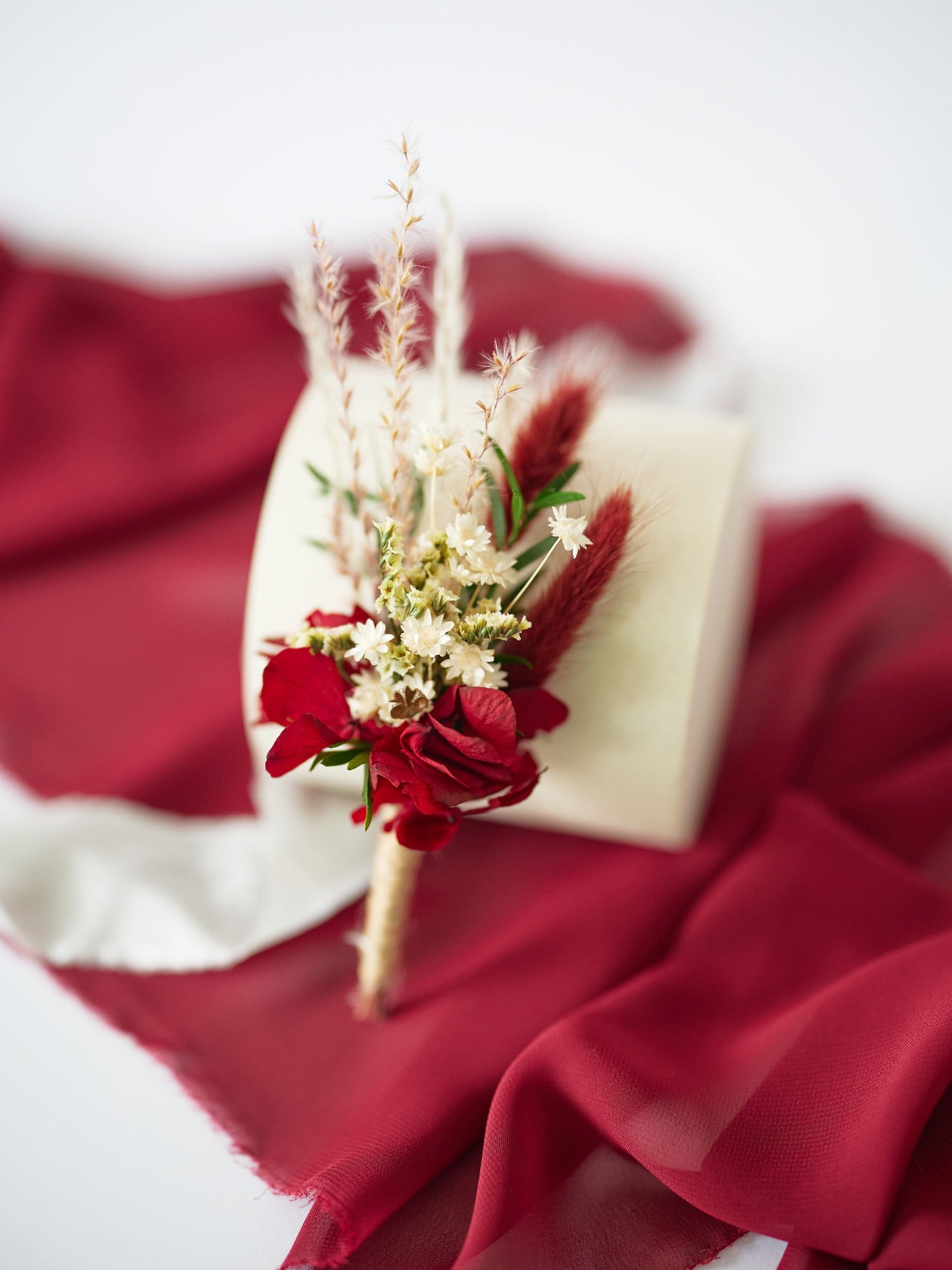 the boutonniere is leaning on a white stand on marsala fabric