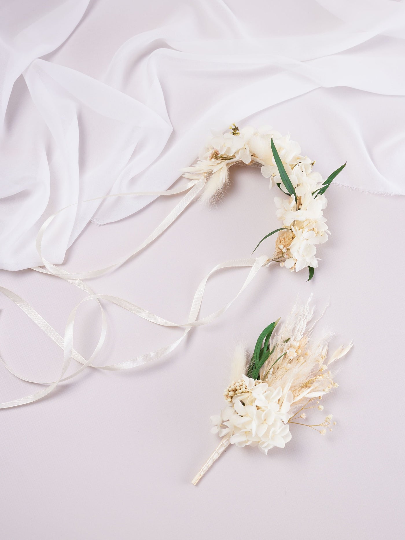 corsage is lying on white background near white organza and wedding boutonniere