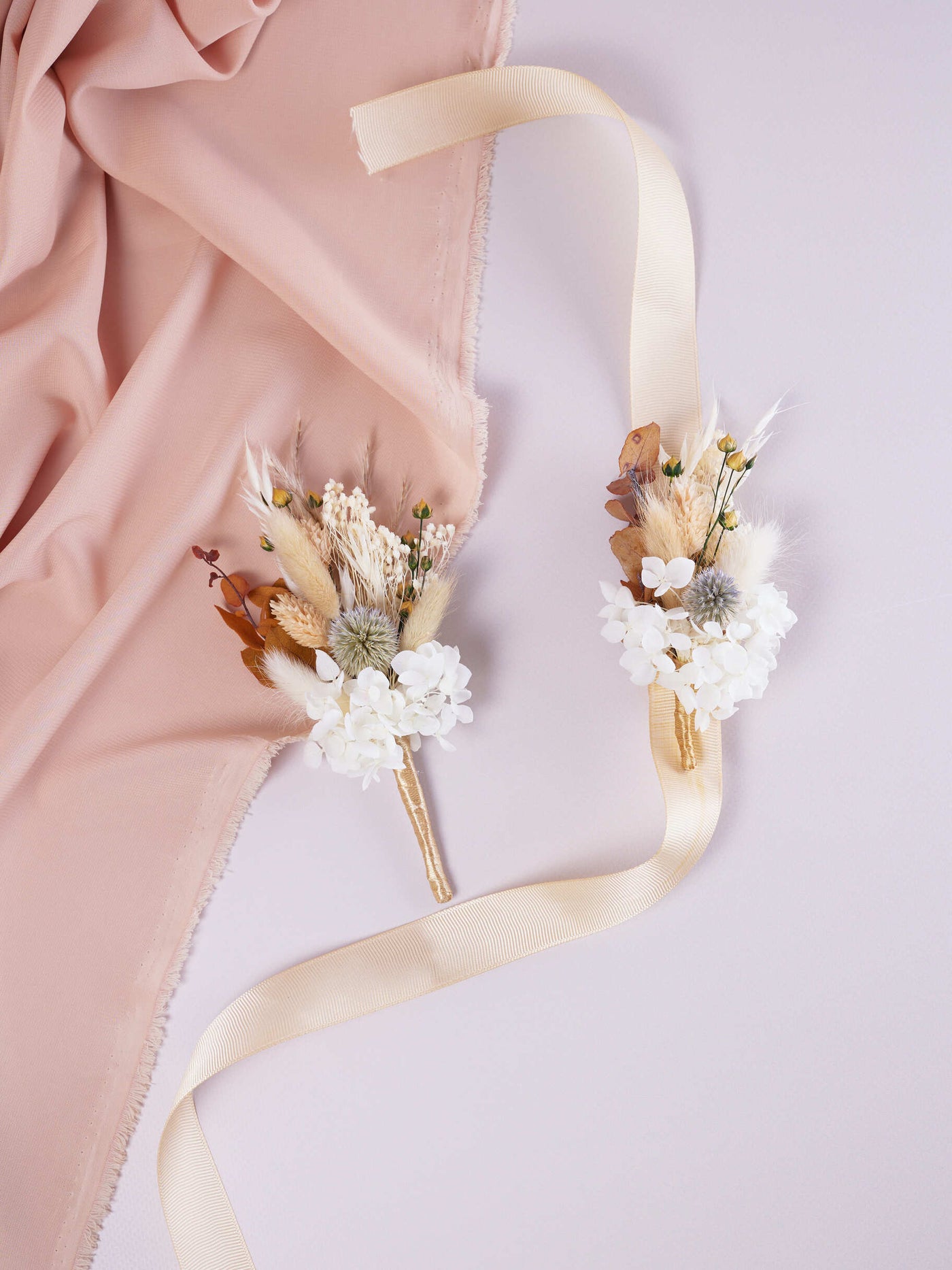 corsage is lying on white background near wedding boutonniere on peach fabric