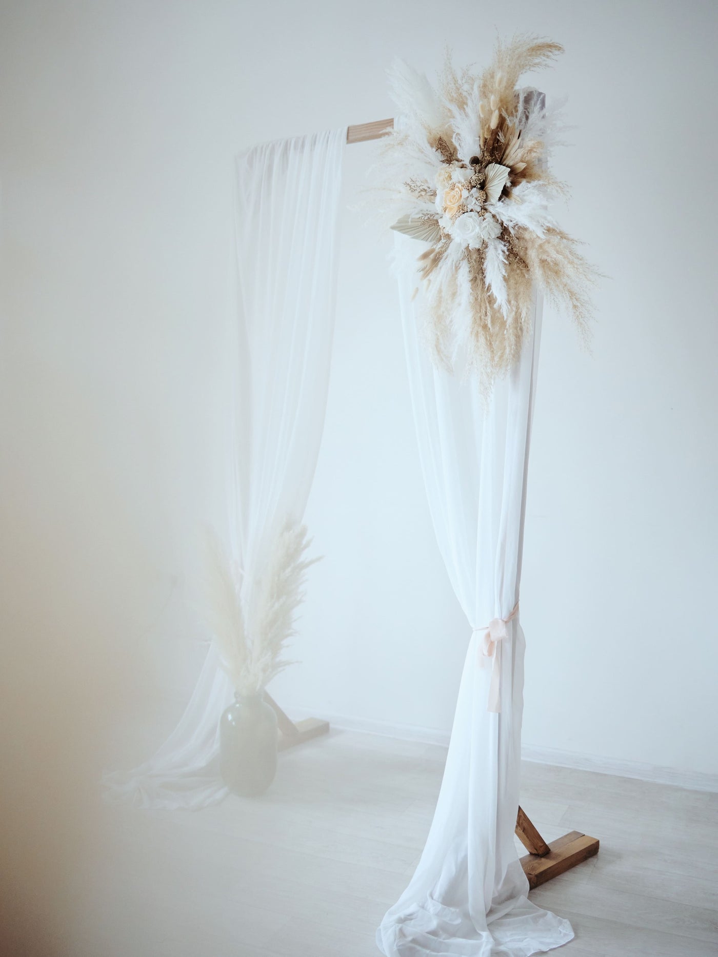 arch flowers bouquet with roses and pampas grass is hanging on wedding arch with white drapes