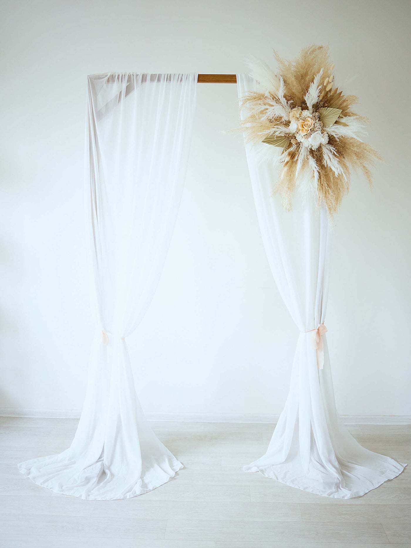 arch flowers bouquet with roses and pampas grass is hanging on wedding arch with white drapes 2