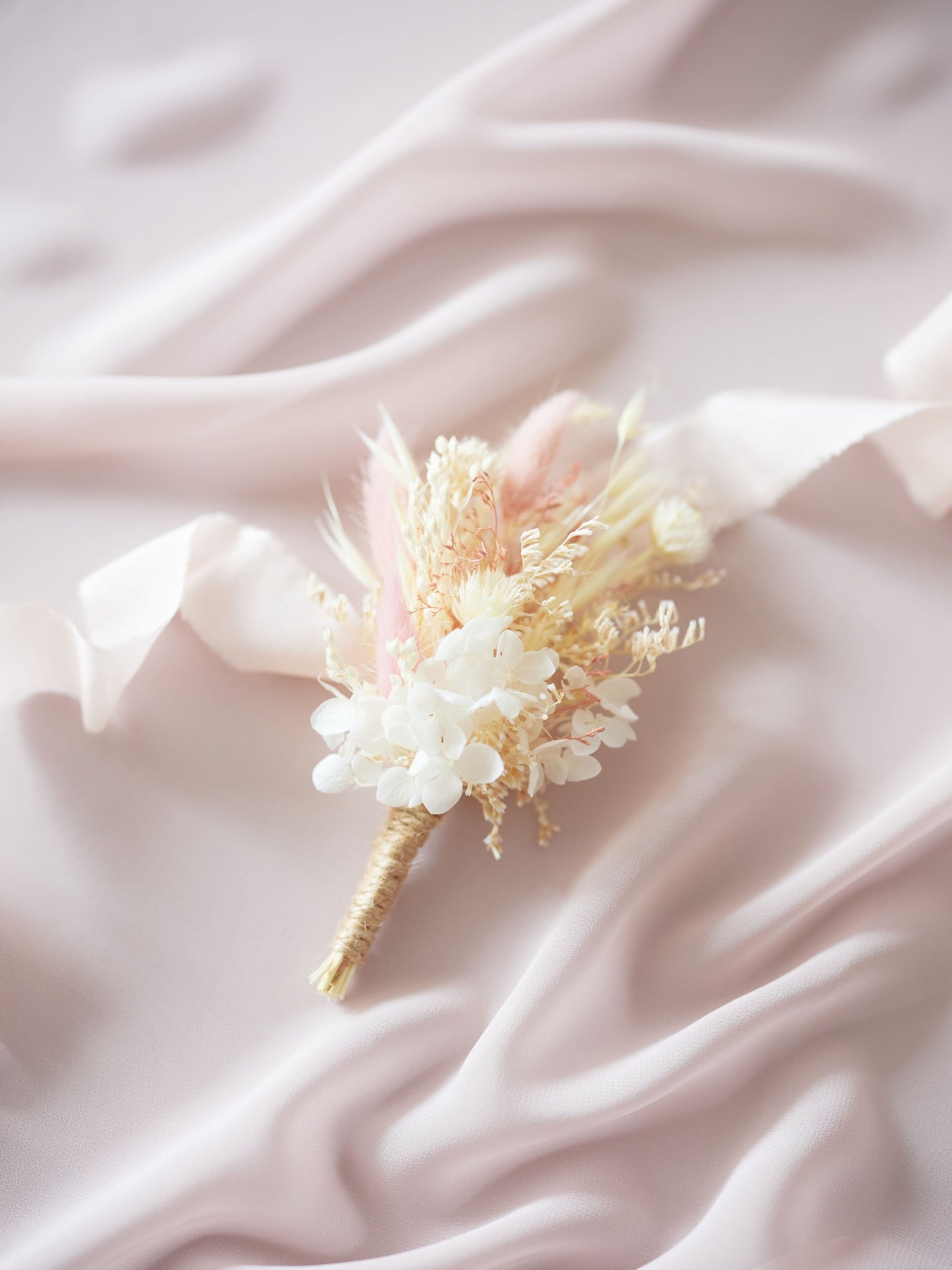 boutonniere is lying on white ribbon and light pink organza