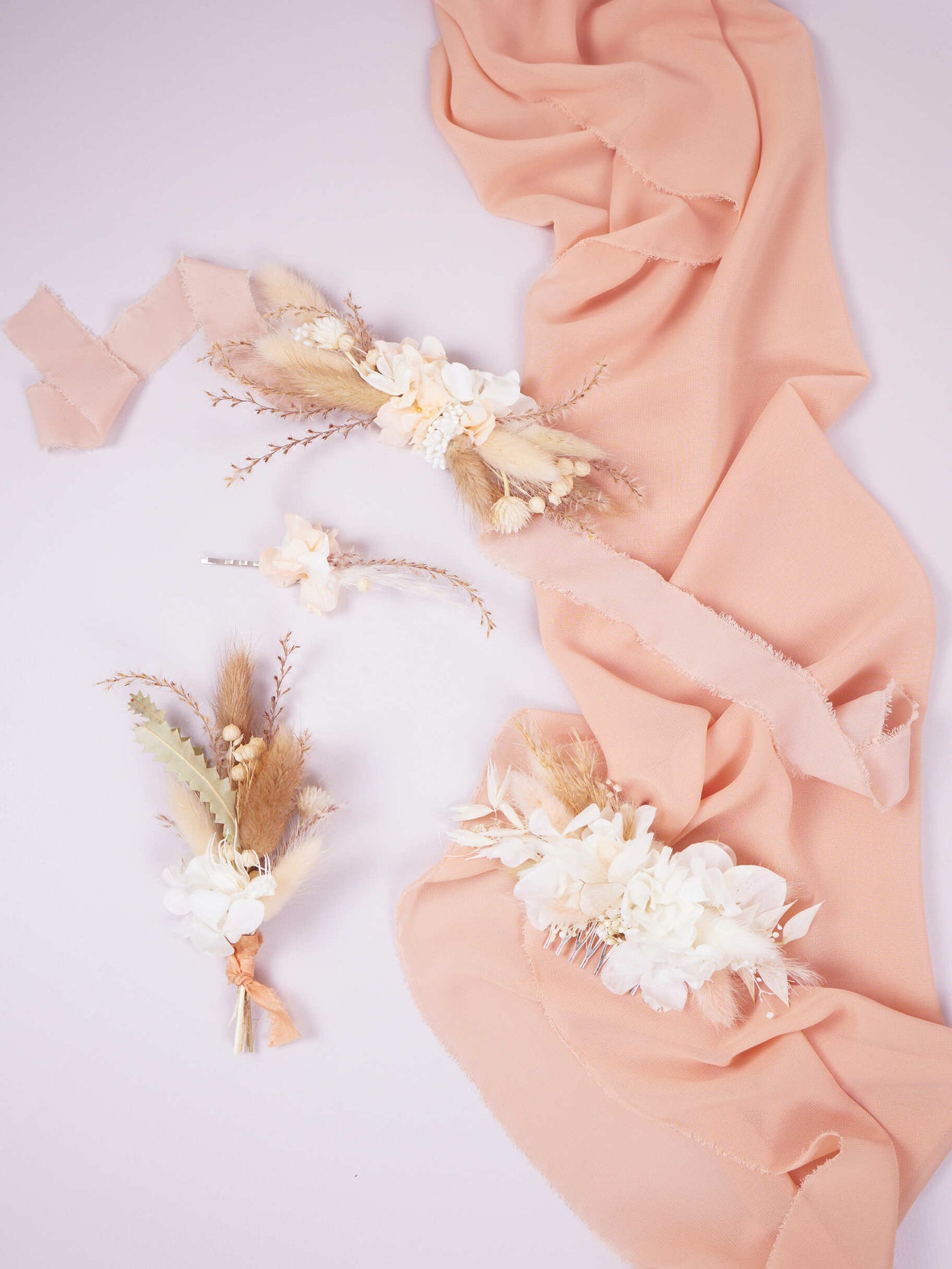 bobby pin is lying near wedding comb, boutonniere, corsage on white background near  pink fabric