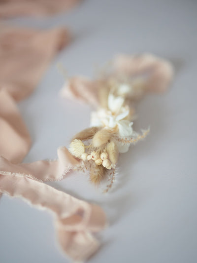 boutonniere is lying on white background near cream ribbon